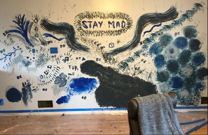 STAY MAD is finger painted on the wall with hundreds of finger strokes encircling it. This invitation hangs above dark blue/black wings and hand prints, swirls, clouds, squiggles in six different shades of deep dark blue. The words 