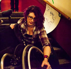 Lindsay sits in an inaccessible stairwell, adjusting the wheel on a wheelchair